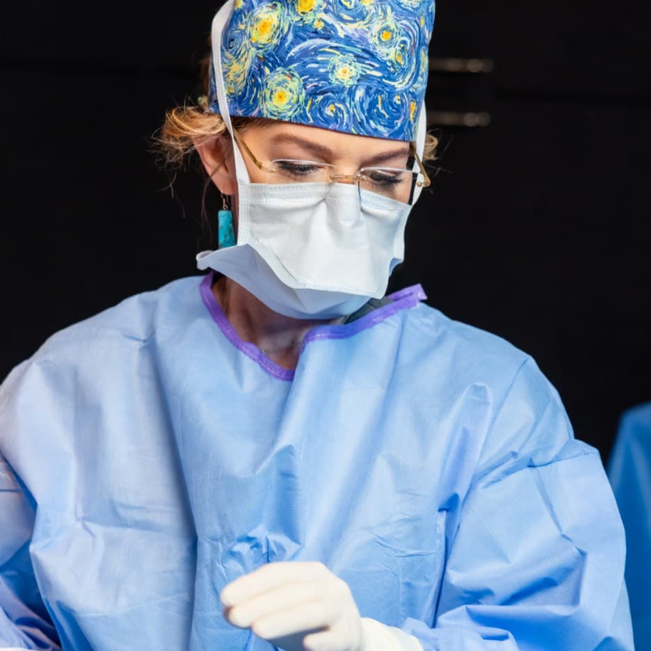 Holly Casey Wall, MD, FACS performing surgery in an operating room wearing a surgical cap and mask.