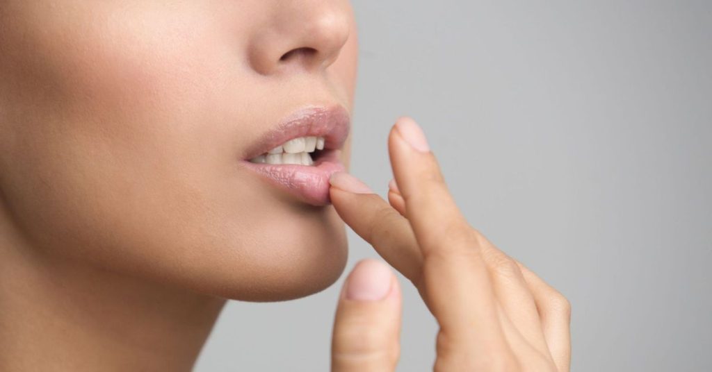 Close-up profile of model's face as she touches a fingertip to her bottom lip.