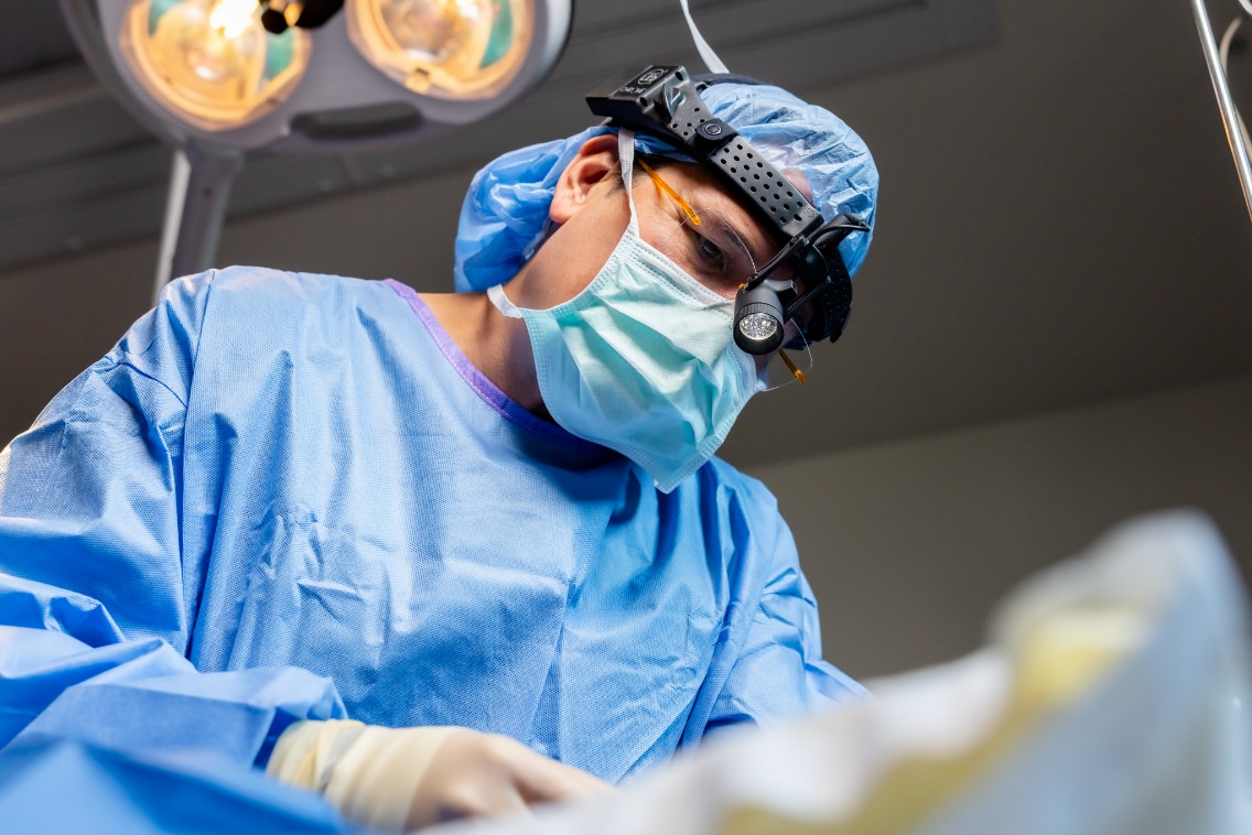 Dr. Wall performing surgery in the operating room wearing surgical scrubs, mask, and magnification loupes