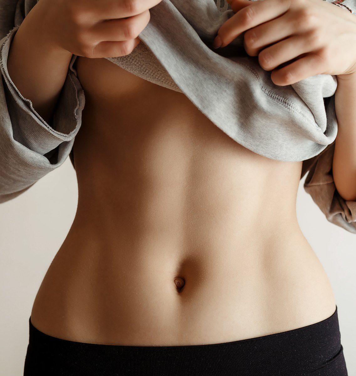 Woman lifting gray shirt to reveal a toned, flat abdomen with defined muscle tone