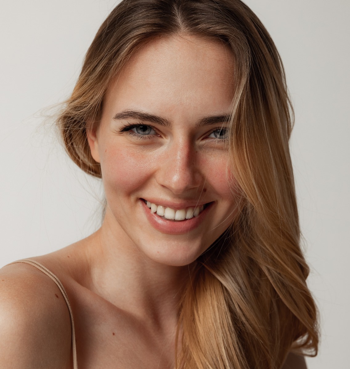 Young woman with strawberry blonde hair and blue eyes smiling warmly with natural, fresh-faced beauty