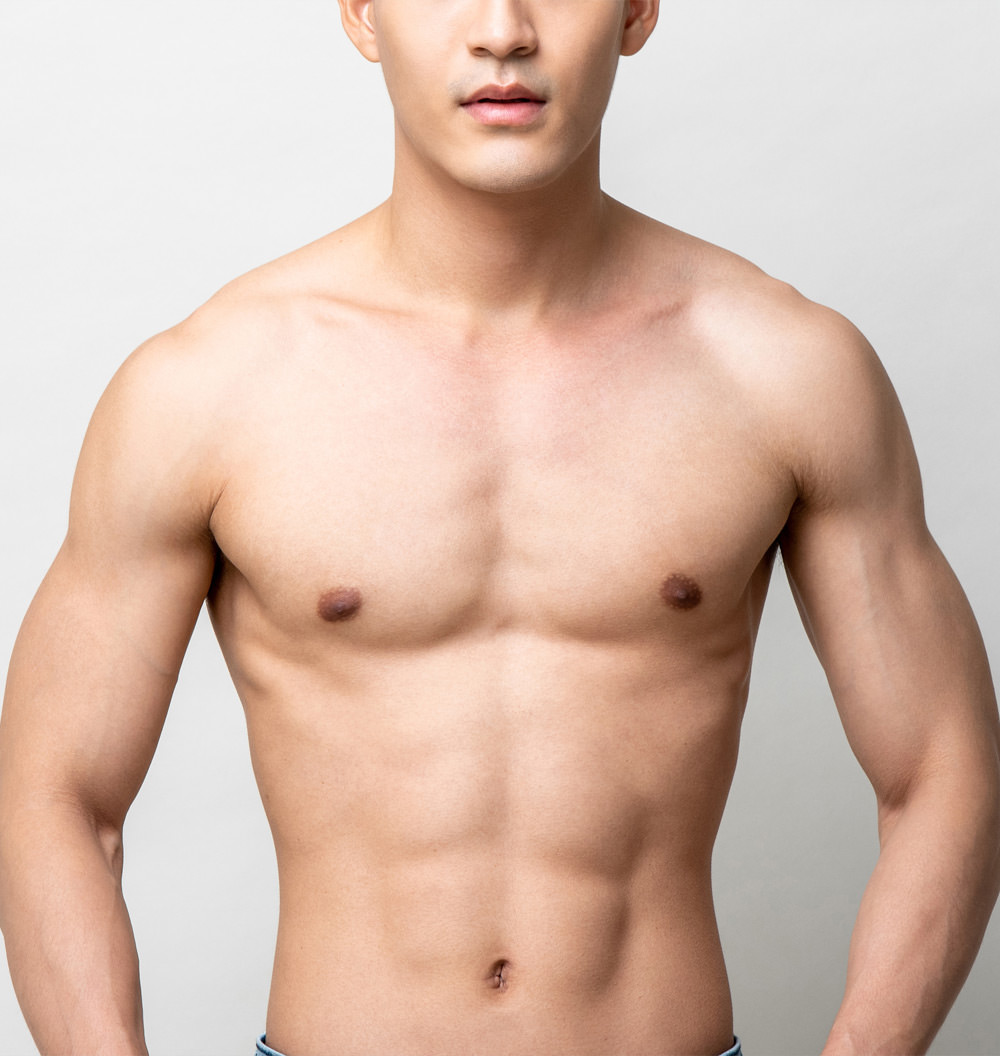 Shirtless athletic man with defined chest, abs, and arms standing against a light gray background